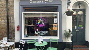 A cafe with a neon sign advertising cocktails, a signboard for Benezers Place, and outdoor seating with green chairs and tables. - Ebenezer's Place (Broadstairs)