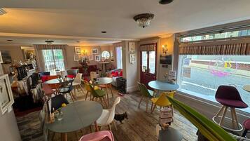 A cozy cafe with wooden floors, colorful chairs, and a variety of seating options including tables and sofas.