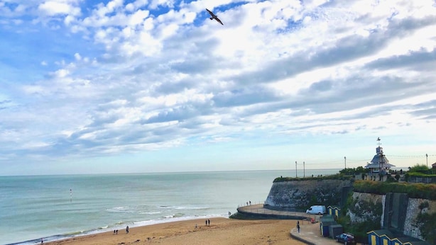 A beach with a clear sky, a few people, and a building with a dome on a cliff. - Ebenezer's Place (Broadstairs)