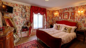 A bedroom with a red bed, a television, a mirror, and patterned wallpaper. - Ebenezer's Place (Broadstairs)