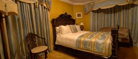 Un dormitorio con una cama grande, una silla de madera y cortinas.