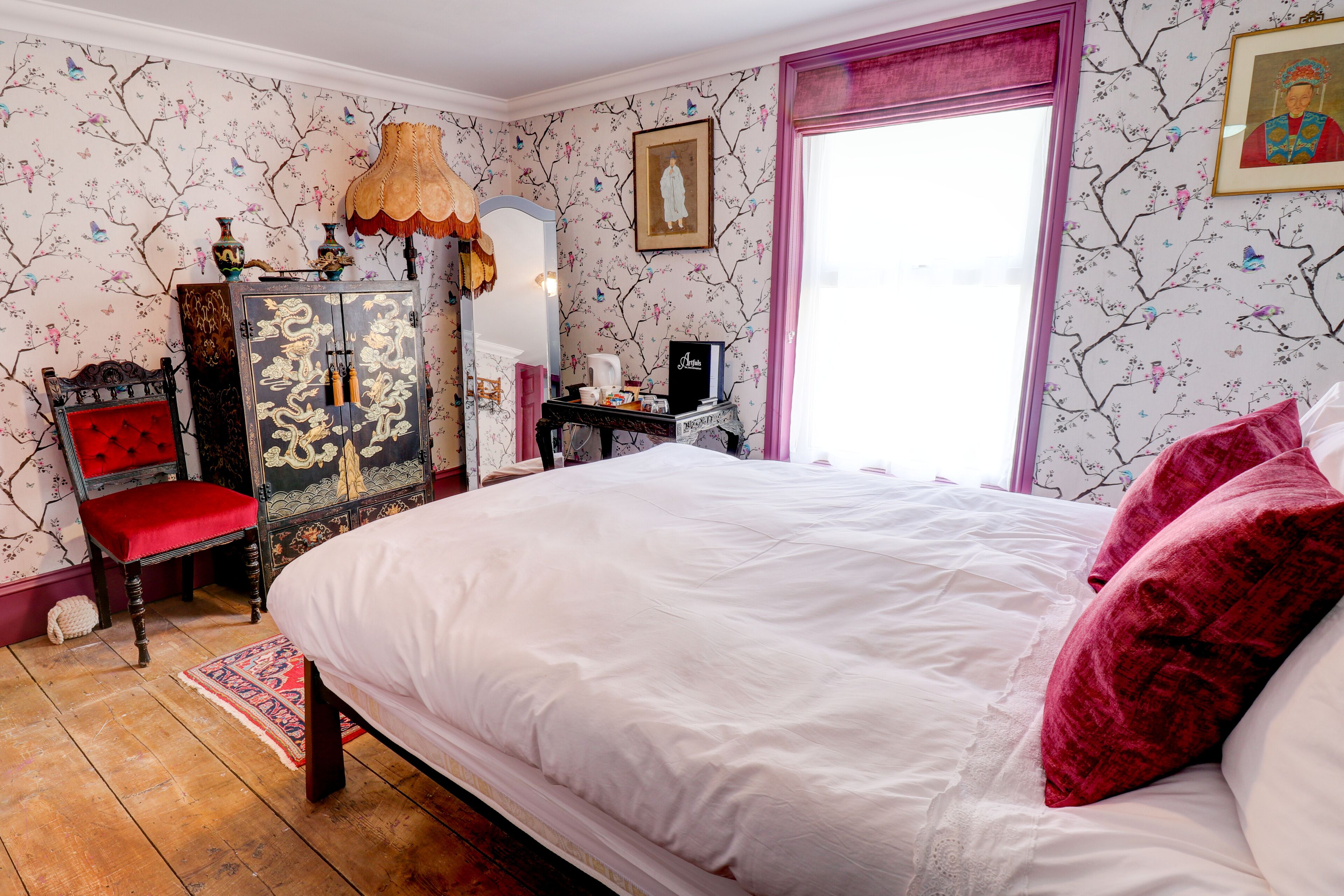 A bedroom with a large bed, a red chair, a wooden cabinet, and a dresser.