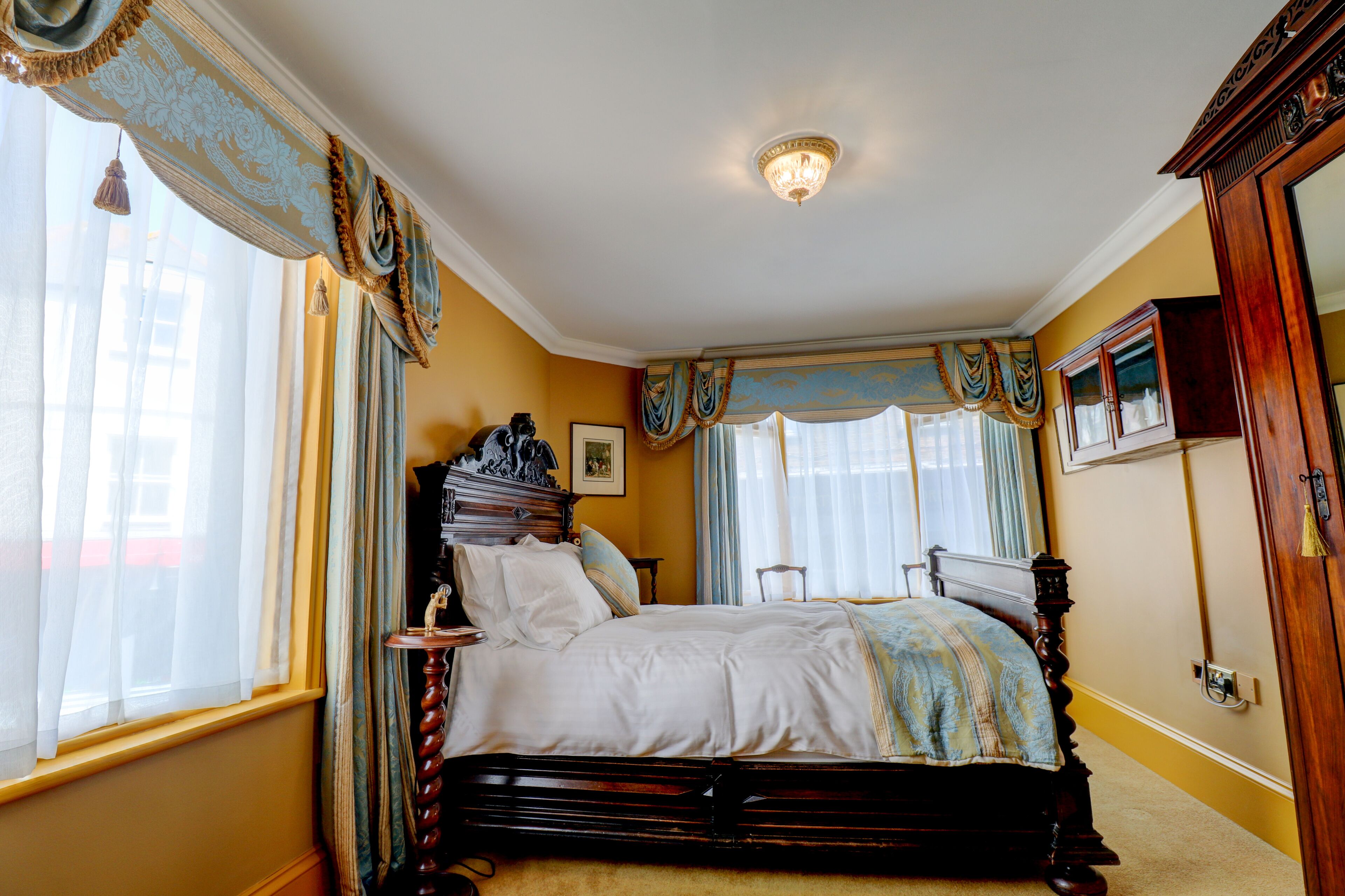 A classic bedroom with a four-poster bed, ornate curtains, and a chandelier.