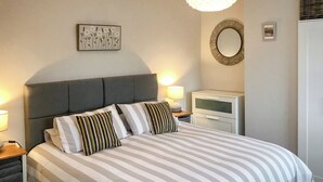 Una cama bien hecha con ropa de cama a rayas, un cabecero tapizado en gris y dos mesitas de noche con lámparas.