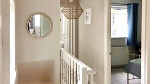 Una escalera con barandillas blancas, un espejo redondo y una lámpara de fibra.