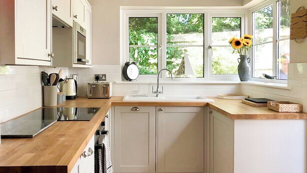 Una cocina con armarios blancos, encimera de madera, un lavamanos y una ventana con vistas a la vegetación.