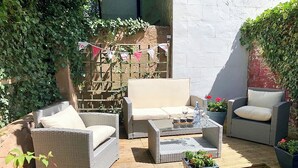 Un patio exterior con mobiliario de mimbre, una mesa de centro de vidrio y plantas en macetas.