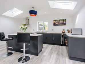 A modern kitchen with a central island, black bar stools, a vase of flowers, and a painting on the wall.