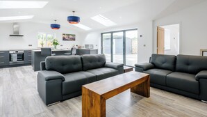 A modern living space with a kitchen, two sofas, a wooden coffee table, and a large sliding glass door to the outside. - 2 bedroom accommodation in Santon Downham (Santon Downham)