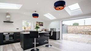 A modern kitchen with a central island, bar stools, and a large window overlooking a garden. - 2 bedroom accommodation in Santon Downham (Santon Downham)