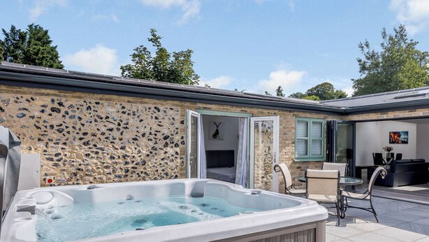 A spa area with a hot tub, a stone wall, a glass door leading to a bedroom, and a seating area with a couch and chairs. - 2 bedroom accommodation in Santon Downham (Santon Downham)