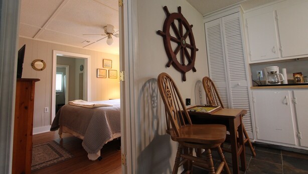A bedroom with a bed, a wooden chair, a dining table, and a ship's wheel decoration. - House with fenced  yard, pets welcome, one level,  Supply, NC (Supply)