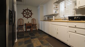 A kitchen with a ship's wheel, two wooden chairs, a refrigerator, and white cabinets. - House with fenced  yard, pets welcome, one level,  Supply, NC (Supply)