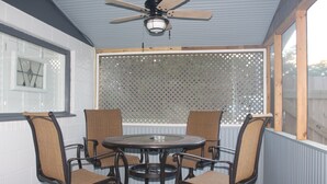 A covered patio with a round table and four chairs, a ceiling fan, and a window with a lattice screen. - House with fenced  yard, pets welcome, one level,  Supply, NC (Supply)
