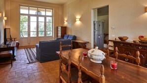 Una cocina amplia con una mesa de comedor, sillas y un refrigerador. Hay un ventanal que proporciona luz natural y vistas a los árboles.