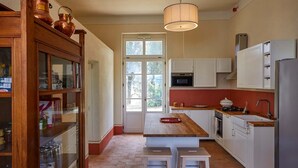 Una cocina con armarios blancos, encimera de madera, lámpara colgante y ventana con vista a árboles.