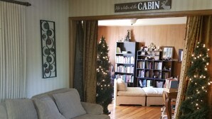 Un accogliente soggiorno con un divano, un tavolino da caffè e una libreria. Ci sono due alberi di Natale e un cartello che dice “La vita è meglio al CABIN”.