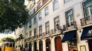 Una calle con tranvía, edificios con balcones y comercios, incluyendo uno llamado 'Cantinho de Cerveja'.