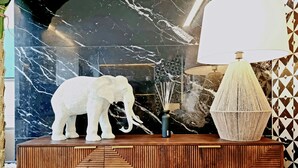 Una consola de madera con un diseño geométrico, una escultura de elefante blanco, una lámpara trenzada y un florero con ramas.