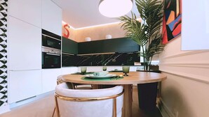 Una cocina moderna con armarios blancos, encimera negra y una mesa redonda de comedor con dos sillas blancas.