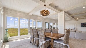 A dining area with a wooden table and wicker chairs, large windows with a view, and a hanging light fixture.