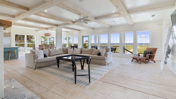 A spacious living area with a high ceiling, large windows, a wooden floor, a sofa, a coffee table, and a chair.