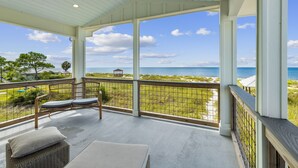 A covered balcony with wicker furniture, a view of the beach, and a clear sky.