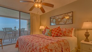 A bedroom with a bed, two bedside lamps, a ceiling fan, and a view of the ocean through a sliding glass door. - Sunset Jetty View! Enjoy one free beach chair set up and umbrella each day! (Destin)