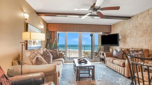 A spacious living room with a large window overlooking the beach, furnished with leather sofas, a coffee table, and a ceiling fan. - Direct Beach Front, High End Vacation,Snow Bird Special WINTER 2027 (St. Augustine)