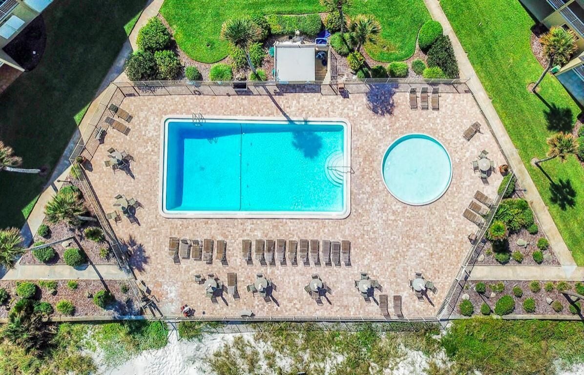 Vue aérienne d’un espace piscine comprenant une piscine rectangulaire, une plus petite piscine circulaire et plusieurs chaises longues disposées autour des piscines.