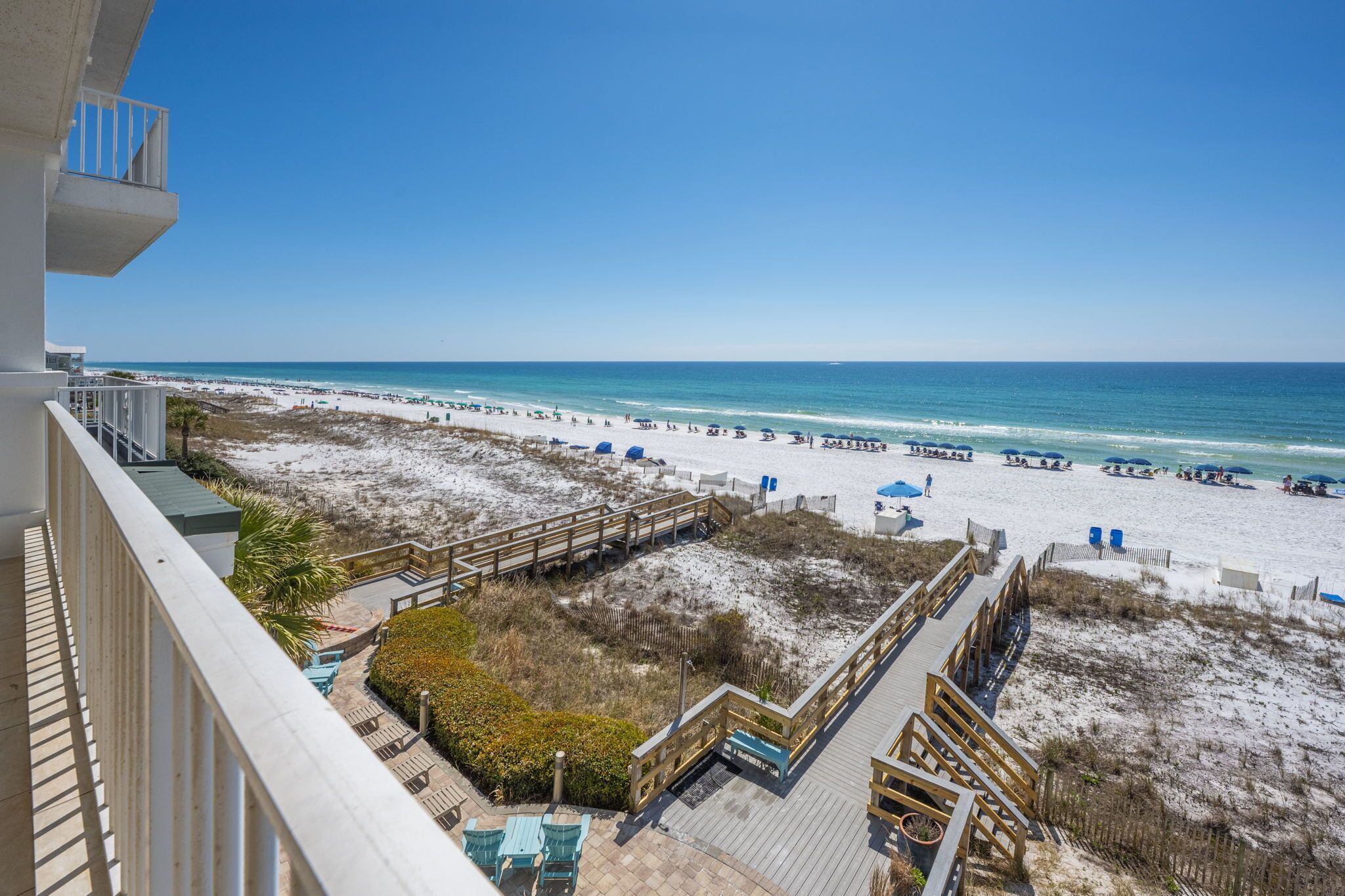 Blick auf einen Strand vom Balkon mit Holzboden, Sandstrand und blauem Himmel.
