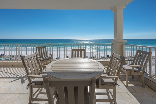 A covered outdoor seating area with a table and chairs, overlooking a beach and ocean.
