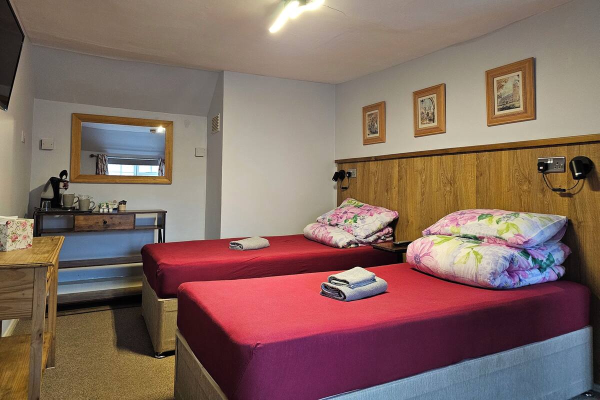 A hotel room with two beds, a wooden headboard, a desk with a chair, a mirror, and framed pictures on the wall.