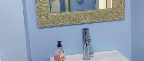 A bathroom with a white sink, a mirror with an ornate frame, and a hand soap dispenser.
