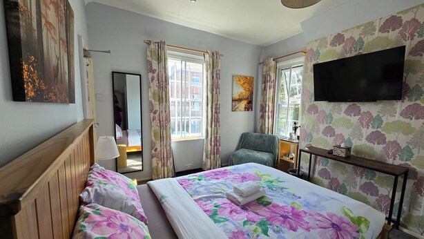 A hotel room with a large bed, two bedside tables, a chair, a TV, and a window with curtains. - Reindeer Accommodation (Southwell)
