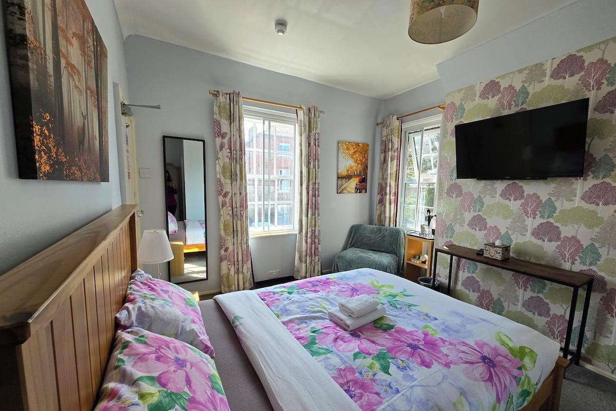 A hotel room with a large bed, two bedside tables, a chair, a TV, and a window with curtains.