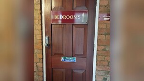 A wooden door with a sign indicating 'BEDROOMS' and a fire exit sign below it. - Reindeer Accommodation (Southwell)