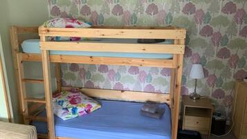A bunk bed with a blue mattress and floral bedding, a wooden nightstand, a lamp, and a patterned wallpaper background.