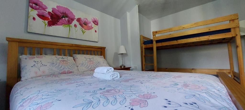 A bedroom with a wooden bunk bed, a floral bedspread, and a painting of flowers on the wall.
