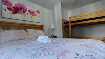 A bedroom with a wooden bunk bed, a floral bedspread, and a painting of flowers on the wall.