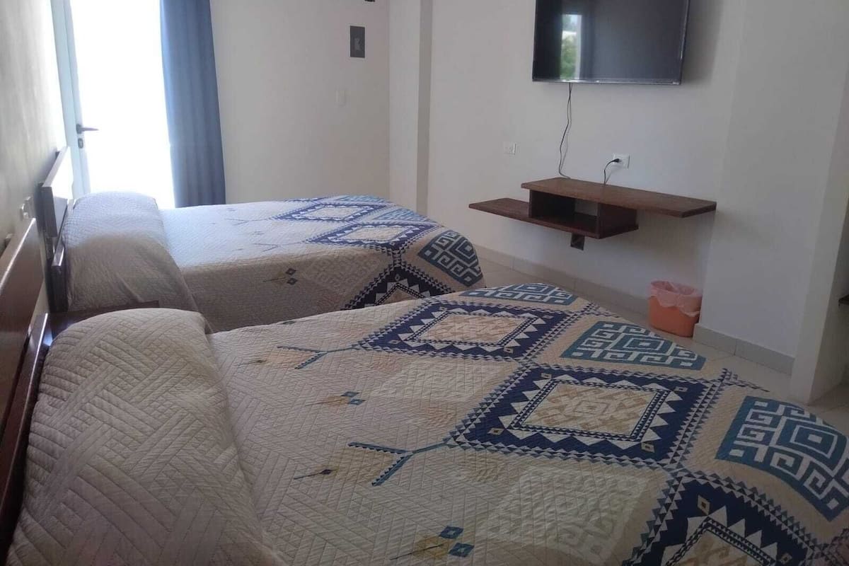 A hotel room with two beds, a TV mounted on the wall, and a small wooden shelf.