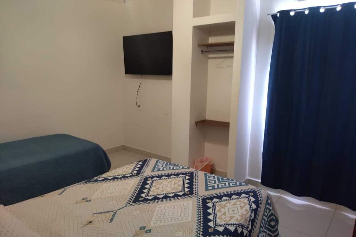 A bedroom with a bed, a television mounted on the wall, a wardrobe, and a curtain.