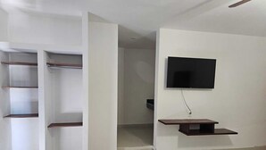 A room with a built-in wardrobe, a flat-screen TV mounted on the wall, and a small wooden shelf. - Hotel Plaza Real La Paz (La Paz)
