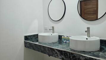 Un baño con dos lavamanos, encimera de mármol y dos espejos redondos.