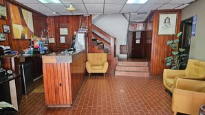 A reception area with a wooden reception desk, a yellow sofa, and a staircase leading to an upper level. - Hotel Plaza Real La Paz (La Paz)
