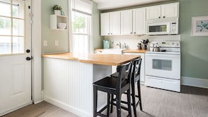 A kitchen with white cabinets, a wooden countertop, a sink, a microwave, and an oven.