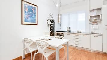 Ett modernt kök med vita skåp, ett matbord med stolar och en inramad tavla på väggen.
