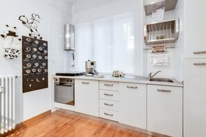 A modern kitchen with white cabinets, a built-in oven, a coffee machine, and a stainless steel range hood.