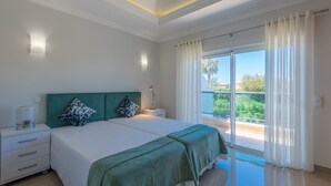 A bedroom with two beds, a nightstand, a lamp, and a view of the outdoors. - Boavista Resort - Casa Belinda (Lagos)