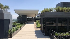 Un edificio moderno con una galería techada, barandillas de metal y vegetación.